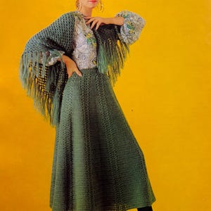 Puede incluir: Una mujer con falda, chal y blusa con estampado floral de ganchillo verde. El chal tiene flecos. Lleva zapatos y medias negras. El fondo es amarillo.