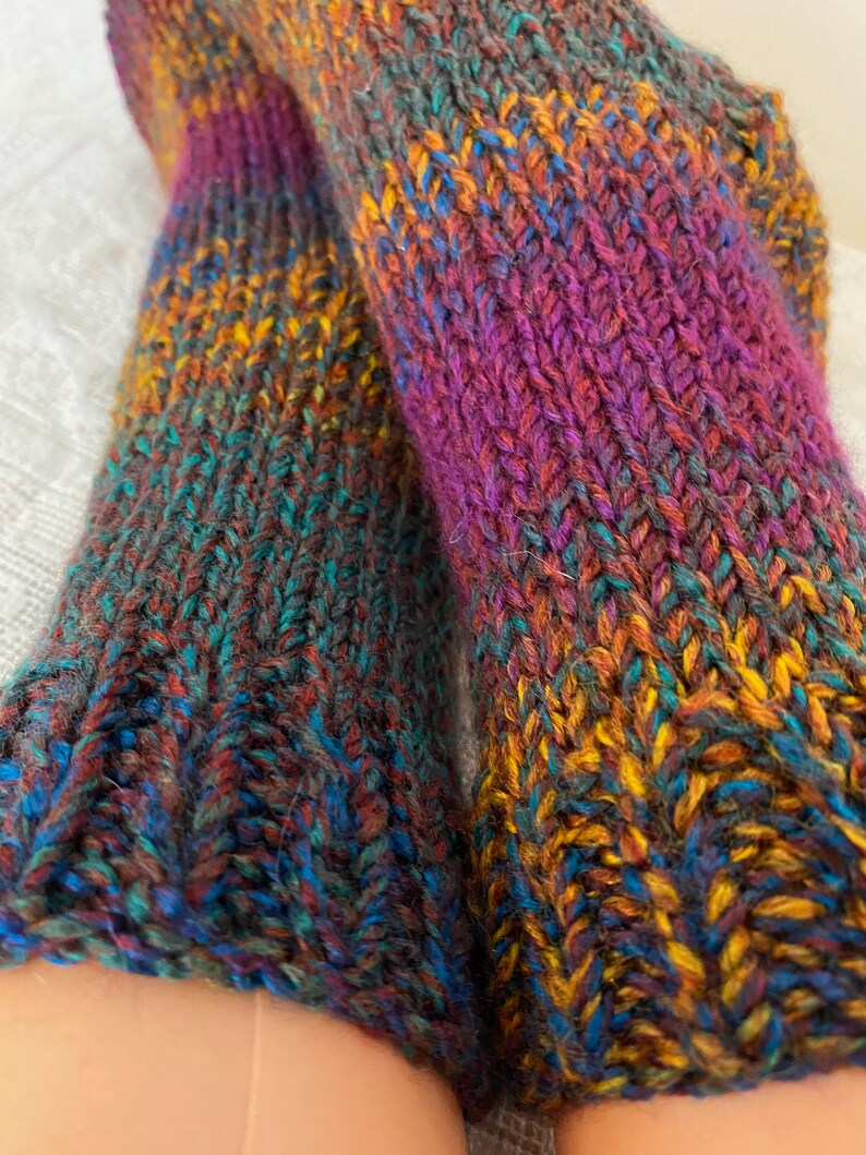 Puede incluir: Un par de calcetines de punto coloridos con un degradado de morado, naranja, azul y verde.