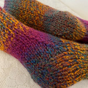 Puede incluir: Un par de calcetines de punto coloridos con un hilo multicolor en tonos de morado, naranja, azul y verde.