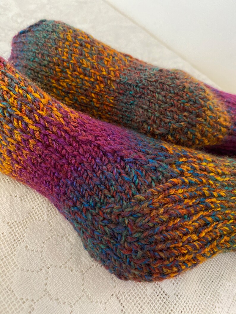 Puede incluir: Un par de calcetines de punto coloridos con un hilo multicolor en tonos de morado, naranja, azul y verde.