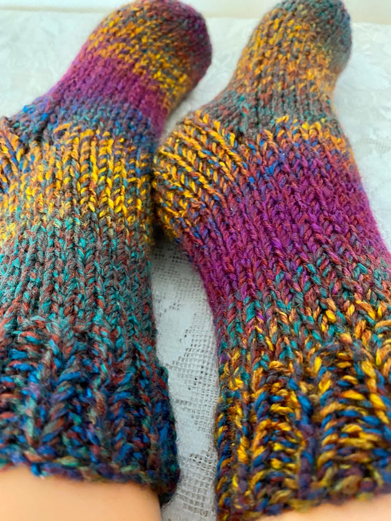 Puede incluir: Un par de calcetines de punto coloridos con un patr&oacute;n degradado en tonos de morado, azul, verde, marr&oacute;n y amarillo.