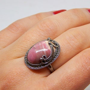 May include: A silver ring with a pink and white oval-shaped gemstone set in a detailed filigree design.