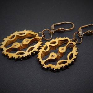 May include: A pair of earrings made from natural materials. The earrings are shaped like a circle with a delicate, intricate design. The earrings are attached to a copper-colored hook.