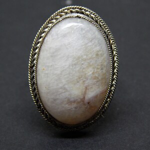 May include: A white oval gemstone ring with a silver braided band.
