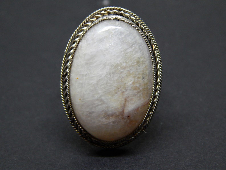 May include: A white oval gemstone ring with a silver braided band.
