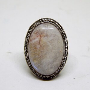 May include: A silver ring with a white oval gemstone set in a braided metal bezel.