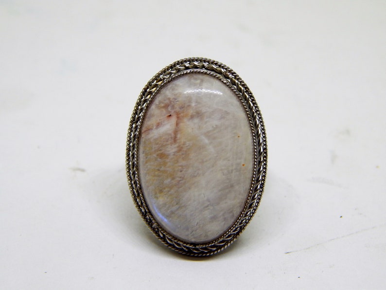May include: A silver ring with a white oval gemstone set in a braided metal bezel.