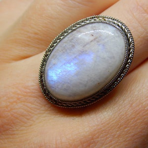 May include: A silver ring with a large oval moonstone. The moonstone is white with a blue iridescent sheen.