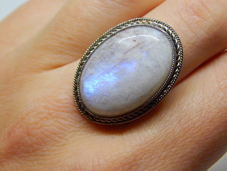 May include: A silver ring with a large oval moonstone. The moonstone is white with a blue iridescent sheen.
