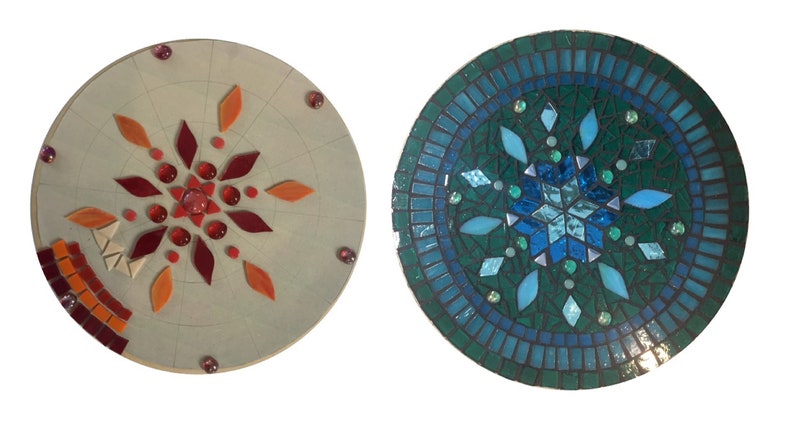 Puede incluir: Dos piezas redondas de arte en mosaico con un dise&ntilde;o de copo de nieve. Una es en tonos de rojo y naranja, la otra es en tonos de azul y verde.