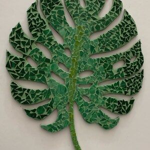 Puede incluir: Una hoja de mosaico verde con un dise&ntilde;o detallado. La hoja est&aacute; hecha de peque&ntilde;os trozos irregulares de vidrio verde.