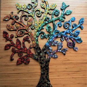 Puede incluir: Un arte de pared de &aacute;rbol de mosaico con un esquema de color arco&iacute;ris. El &aacute;rbol est&aacute; hecho de peque&ntilde;as baldosas de vidrio de colores y tiene un dise&ntilde;o caprichoso y org&aacute;nico.