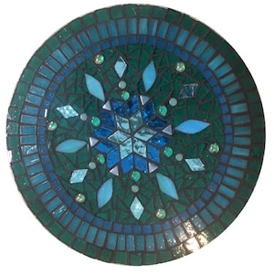 Puede incluir: Una baldosa redonda de mosaico con un dise&ntilde;o de copo de nieve en tonos azules y verdes. El copo de nieve est&aacute; rodeado por un borde de baldosas m&aacute;s peque&ntilde;as en tonos azules.
