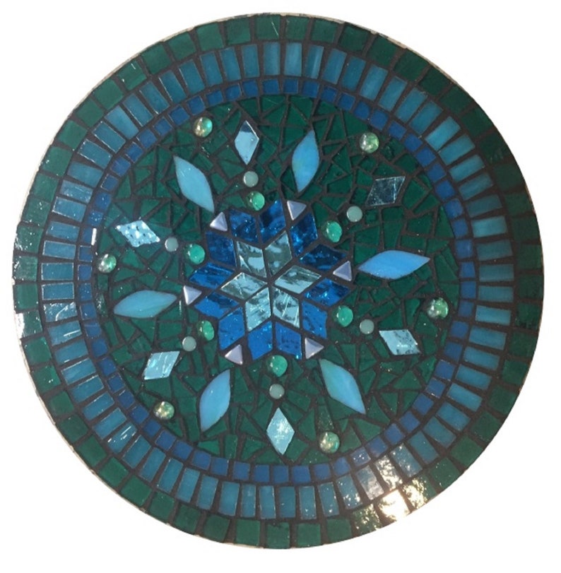 Puede incluir: Una baldosa redonda de mosaico con un dise&ntilde;o de copo de nieve en tonos azules y verdes. El copo de nieve est&aacute; rodeado por un borde de baldosas m&aacute;s peque&ntilde;as en tonos azules.