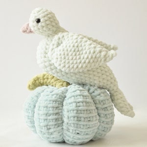May include: A white crocheted bird perched on top of a light blue crocheted pumpkin. Both are made with a fluffy yarn.