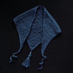 May include: A blue crocheted scarf with a tassel and a bead. The scarf is folded in a triangular shape and has a long, flowing design.