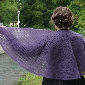 May include: A purple crocheted shawl with a lacy pattern. The shawl is draped over the shoulders of a person standing outdoors.