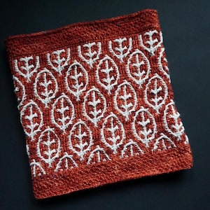 Könnte beinhalten: Nahaufnahme eines roten gestrickten Stoffes mit einem weißen Blatt-Muster. Der Stoff ist strukturiert und hat eine leicht raue Oberfläche.