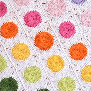 May include: A white crocheted blanket featuring colourful circular motifs in shades of pink, orange, yellow, green and blue.