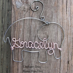 May include: A gray wire elephant ornament with the name "Gracelyn" written in pale pink wire.