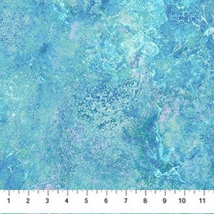 May include: A close-up of a fabric with a marbled design in shades of blue and teal. The fabric has a textured appearance, with lighter and darker areas creating depth. A ruler is at the bottom, showing measurements up to 12 inches.