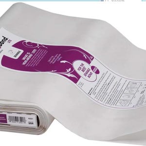 Pode incluir: Um rolo de tecido de entretela fusível HeatnBond Lite. O tecido branco está parcialmente desenrolado, revelando um rótulo roxo e branco com informações do produto. O rolo é rotulado "HeatnBond Lite".
