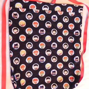 May include: Black fabric tote bag with a repeating pattern of cartoon superhero characters in white circles. The bag has red straps and a simple design. The bag is made of fabric.