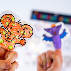 May include: Two finger puppets, one orange with green polka dots and an elephant design, the other purple with a bat design.