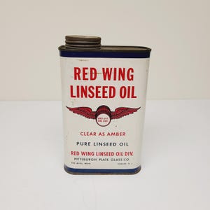 May include: A vintage tin can of Red Wing Linseed Oil. The can is white with red and blue accents. It features a red wing logo with the text "REG.U.S. PAT OFF." The can also says "CLEAR AS AMBER PURE LINSEED OIL RED WING LINSEED OIL DIV. PITTSBURGH PLATE GLASS CO. RED WING, MINN. NEWARK, N.J."
