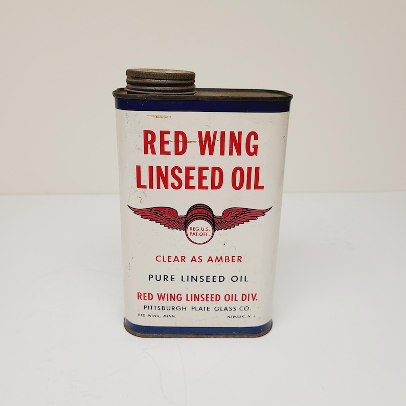 May include: A vintage tin can of Red Wing Linseed Oil. The can is white with red and blue accents. It features a red wing logo with the text "REG.U.S. PAT OFF." The can also says "CLEAR AS AMBER PURE LINSEED OIL RED WING LINSEED OIL DIV. PITTSBURGH PLATE GLASS CO. RED WING, MINN. NEWARK, N.J."