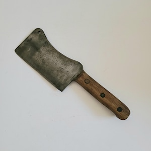 May include: A vintage cleaver with a curved blade and a wooden handle. The blade is made of metal and has a dull finish. The handle is brown and has a worn look.