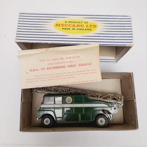 May include: A Dinky Supertoys B.B.C. TV extending mast vehicle in a cardboard box with a Meccano Ltd label. The green and white toy truck features a metal extending mast on top and includes an instruction sheet mentioning a 20 inch cord.