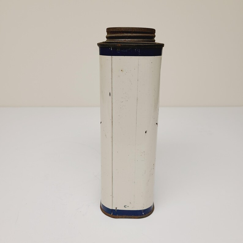 May include: White metal tin with a blue band around the top and bottom. The tin has a rusty metal lid.