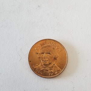 May include: A gold-colored coin with a portrait of Kit Carson on the front. The coin has the words "Kit Carson" around the edge.