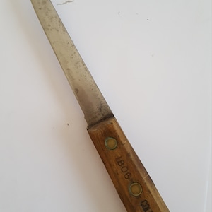 May include: A vintage knife with a worn, stainless steel blade and a wooden handle. The handle is marked with the text "1806" and "COLUMBIA". The knife is likely used for cutting and food preparation.