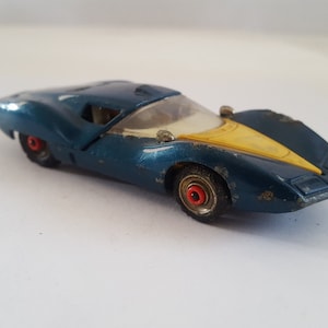 May include: A blue and yellow toy car with red wheels. The car has a white windshield and a yellow stripe on the hood.