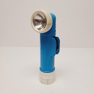 May include: A vintage blue and white flashlight with a ribbed body. The flashlight has a white bezel around the light and a black clip on the side. The base of the flashlight is also white.