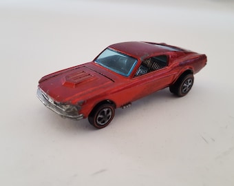 May include: A red toy car model of a Ford Mustang. The car has a black interior and black wheels.