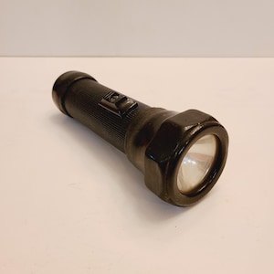 May include: A black flashlight with a ribbed body and a round, slightly angled head. The flashlight has a simple on/off switch.