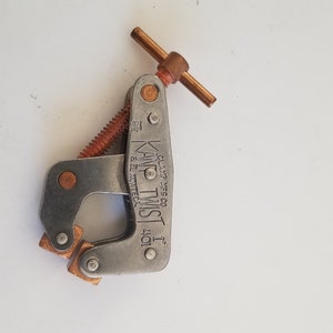 May include: A silver metal clamp with a copper-colored handle and screw. The clamp is labeled "KNOT-TWIST 1" and "GLAZE WIRES CO."
