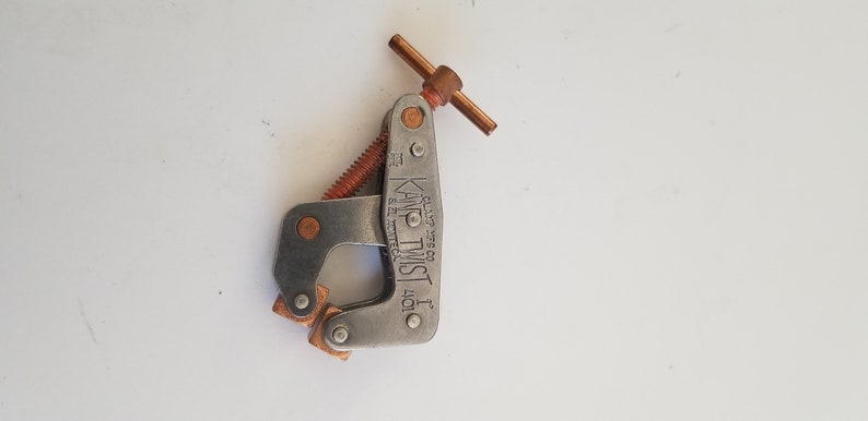 May include: A silver metal clamp with a copper-colored handle and screw. The clamp is labeled "KNOT-TWIST 1" and "GLAZE WIRES CO."