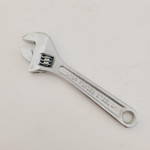 May include: A silver adjustable wrench with the text "DROP FORGED STEEL 4" on the handle. The tool is designed for tightening or loosening nuts and bolts. The wrench is made of steel and has a smooth, shiny finish.