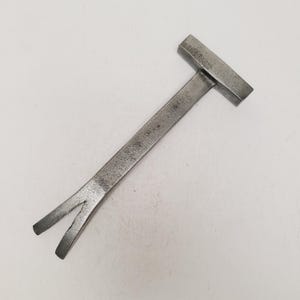 May include: A dark gray metal pry bar featuring a flat, T-shaped head at one end and a V-shaped, bifurcated claw at the opposite end. The tool has a textured, matte finish and a straight, elongated shaft connecting the two functional ends.