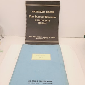 May include: Two manuals are displayed. The top manual is black with gold lettering and reads "AMERICAN BOSCH FUEL INJECTION EQUIPMENT MAINTENANCE MANUAL." The bottom manual is light blue with a yellow label. The text "NAVY DEPARTMENT - BUREAU OF SHIPS" is visible.
