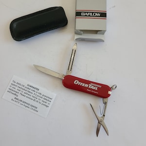 May include: A red pocket knife with a silver blade and a black leather case. The knife has the words "Otter Tail Power Company" printed on the side. The knife also has a small pair of scissors attached to it.
