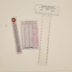 May include: Three rulers, one with a white background and black markings, one with a white background and red and black markings, and one with a white background and a chart of decimal equivalents. The ruler with the chart has the text "DECIMAL EQUIVALENTS" and "THE CLEVELAND TWIST DRILL CO."