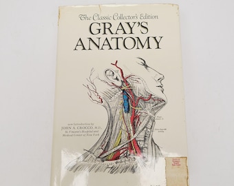 May include: A hardback book titled The Classic Collector's Edition Gray's Anatomy with a white cover featuring a detailed anatomical line drawing of the human neck and head, including red, blue, and yellow highlights and 780 illustrations.