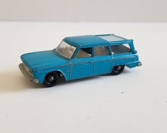 May include: A blue toy car model of a station wagon. The car has a white roof and black wheels.