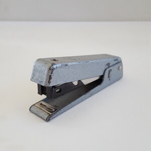 May include: A silver metal stapler with a black plastic staple remover. The stapler is in a slightly used condition.