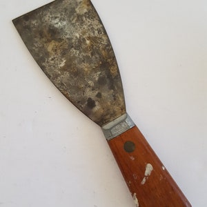 May include: A metal putty knife with a wooden handle. The blade is rusty and the handle has white paint splatters.